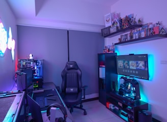 A modern gaming setup featuring a sleek gaming chair, dual monitors on a desk, and LED lighting. A gaming console and various decorations are displayed on shelves, creating an organized and vibrant gaming environment.