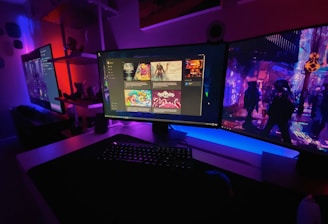A gaming setup featuring multiple screens with vibrant game-related images illuminated by colorful LED lighting. The environment is dimly lit, highlighting the vivid displays on the monitors. A keyboard is visible on the desk beneath the central monitor.