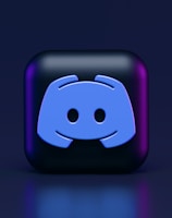 A 3D-style block with a blue logo in the center, set against a dark background. The logo resembles a game controller with two rounded edges and two circles on the front. The block has a subtle gradient, transitioning from dark to purple on its sides.